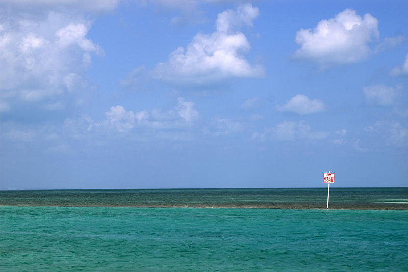 a small sign and a big blue horizon, no wake zone inside a coral reef